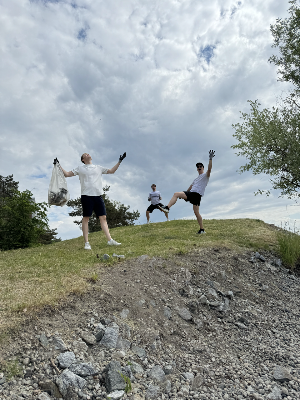 3 happy people standing on a hill with trash bags and gloves ready for the beach cleanup